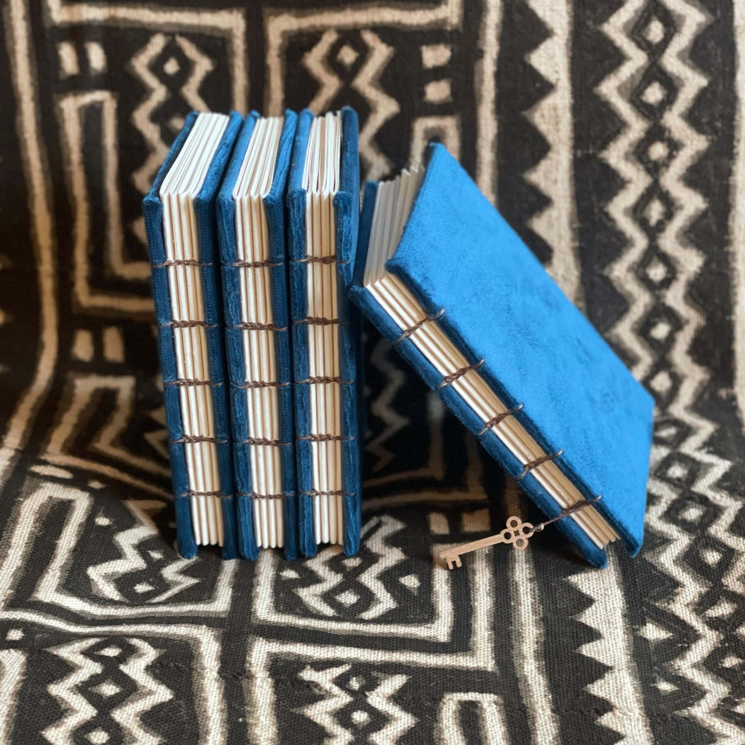 This is an image of handmade sketchbooks. This particular image features four of them standing upright against an African patterned blanket